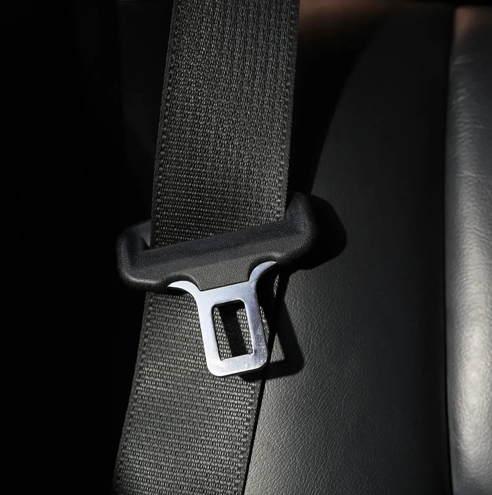 Seat belt latch plate resting against dark upholstery, showing the webbing loop and metal tongue.