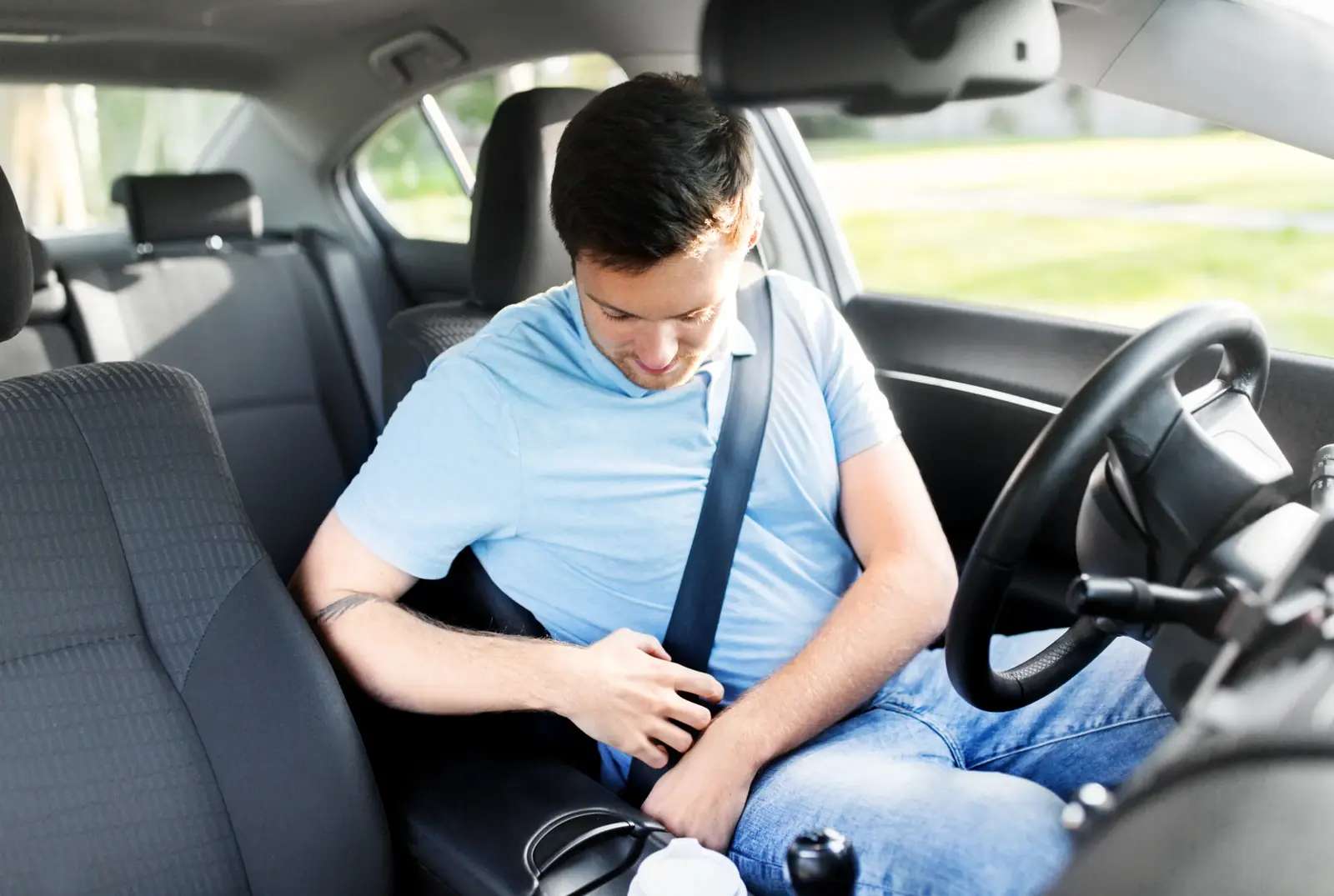 Occupant in a passenger car fastening a three-point seat belt across the chest and lap.