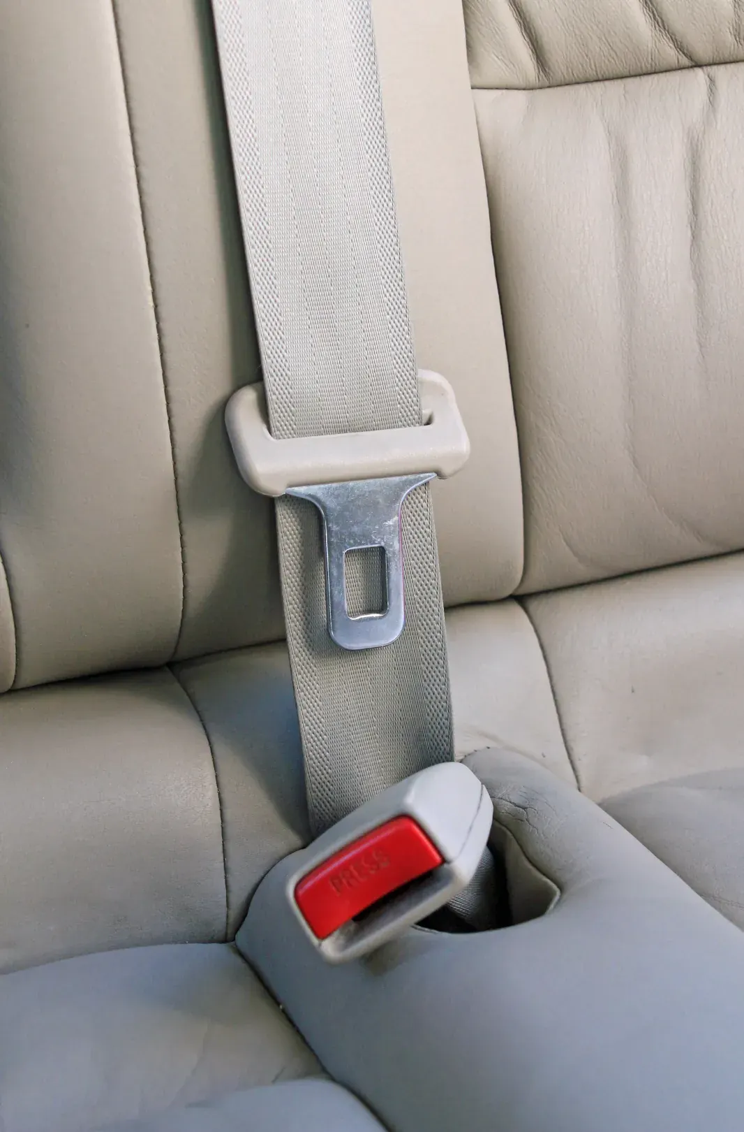Three-point seat belt webbing and buckle running across a light-coloured vehicle seat.