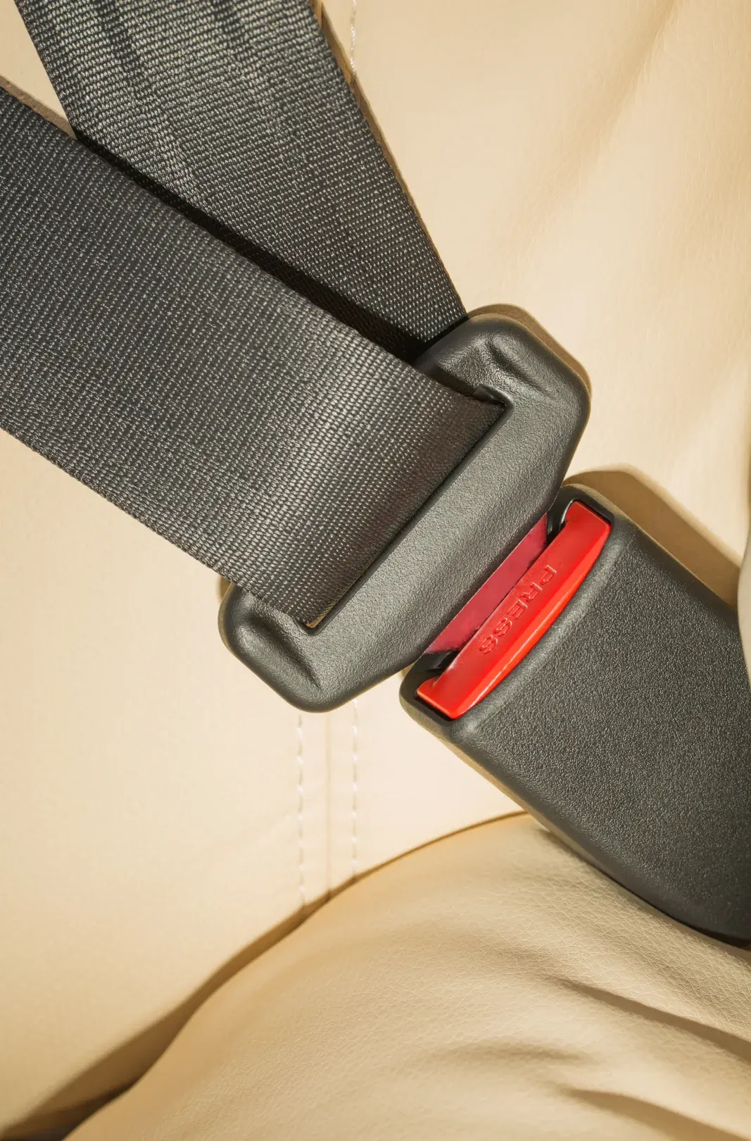 Seat belt webbing routed over a light-coloured vehicle seat toward the buckle.