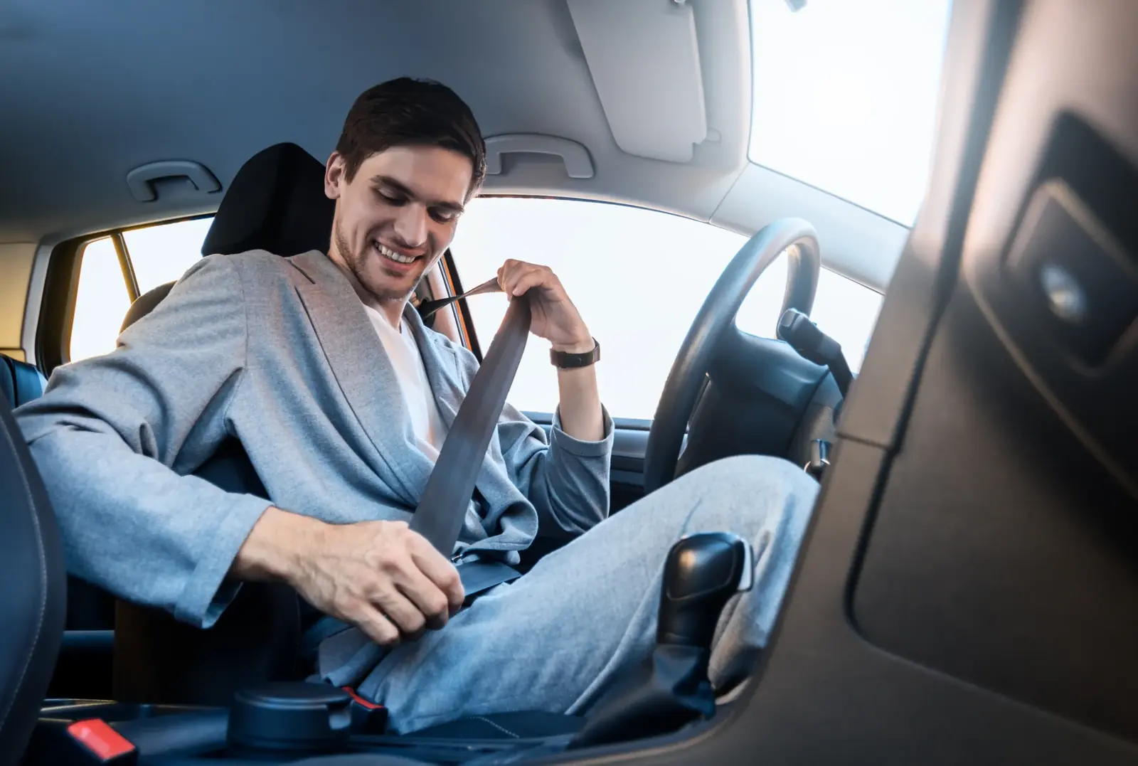 Driver seated in a car cabin reaching across to draw the seat belt over the shoulder.
