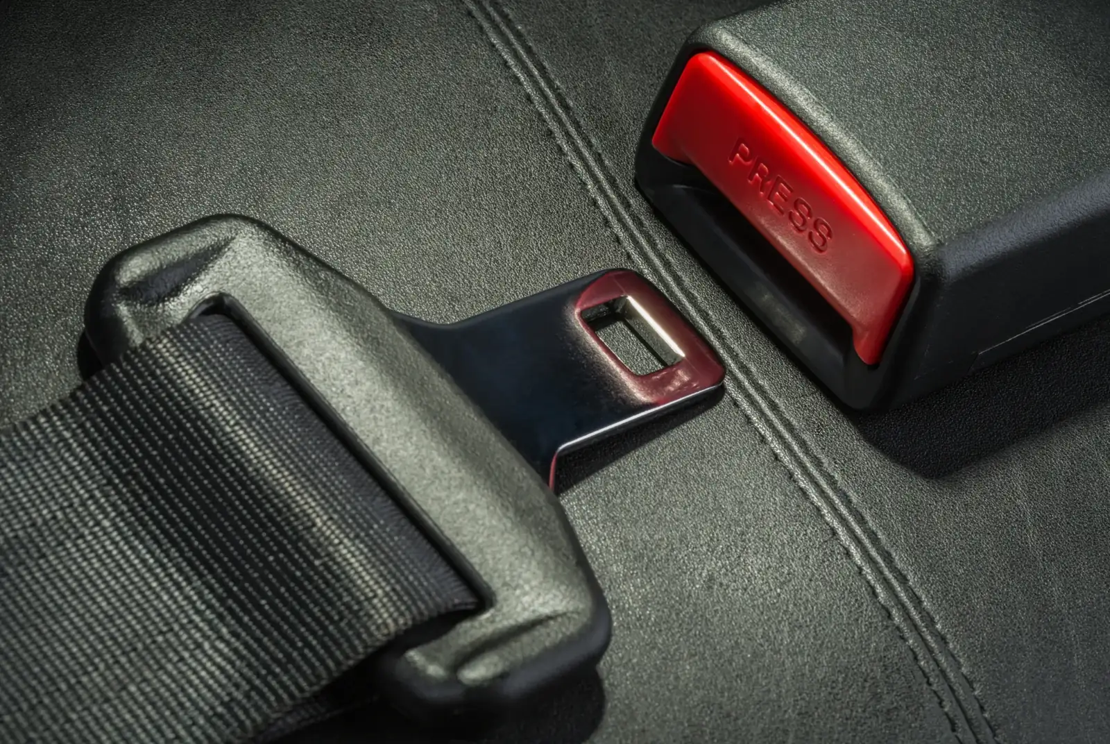 Detailed view of a seat belt buckle housing and latch plate seated on dark vehicle upholstery.