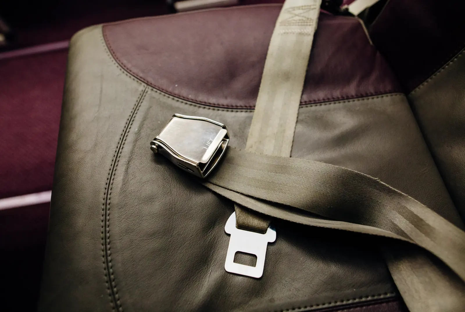 Two-point lap belt with a lift-lever metal buckle lying across a seat.
