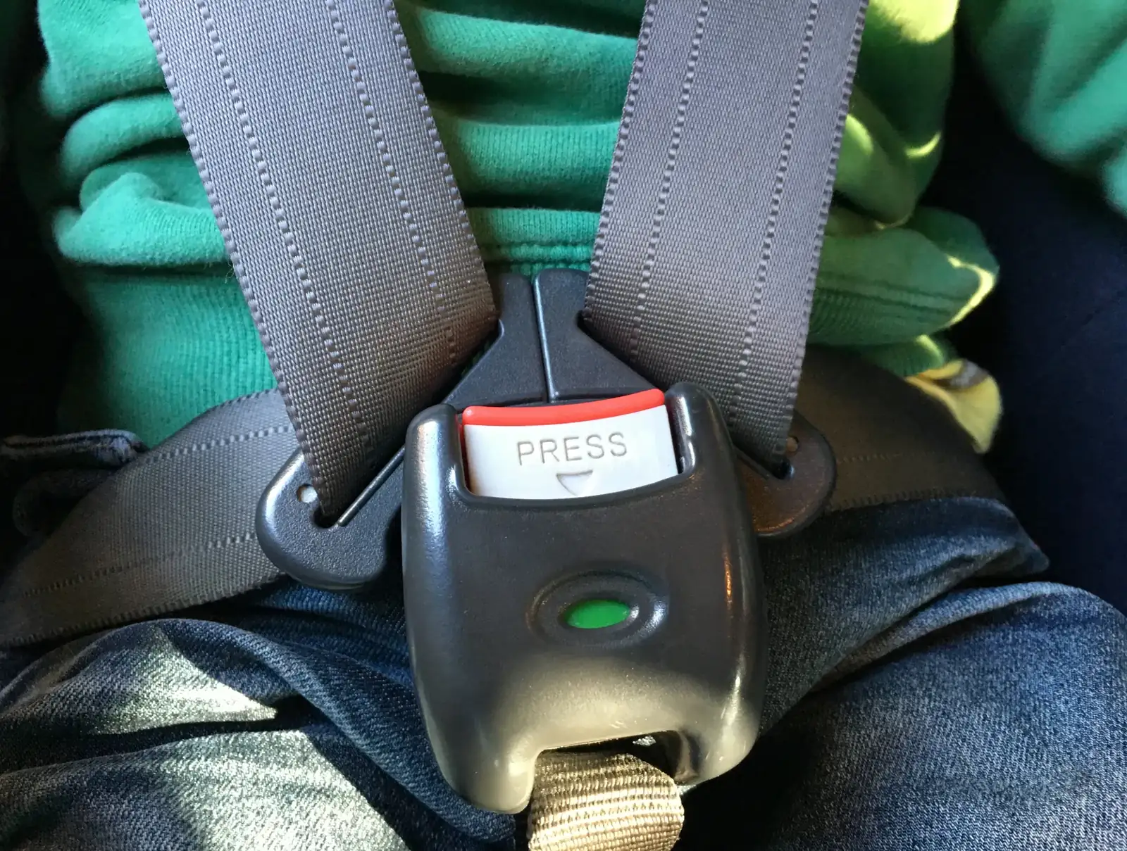 Child restraint harness straps meeting at a central buckle across a seated child.
